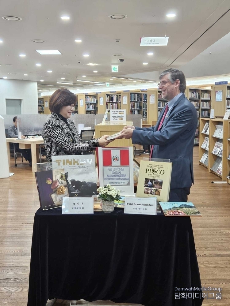 Oh Ji-eun, director of the Seoul Library (left) receives a book from Peruvian Ambassador to Korea Paul Duclos on Feb. 16. The Seoul Library received a donation of 20 books from the Peruvian Embassy in Seoul, which include introductions to Peru's history, culture, and locales. / Courtesy of the Peruvian Embassy