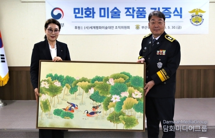 Lee Mi-hyung, director of the K Folk Painting Research Center and professor at Myongji University's K-Folk Painting Department (left), presents her artwork to Nam Joon-rak, chief of the Busan Detention Center.